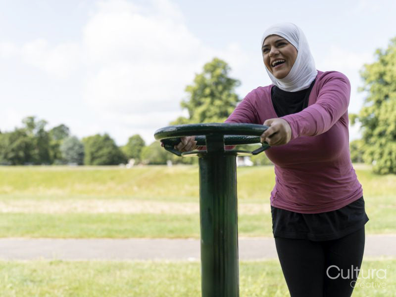 Sutton,Smiling woman in headscarf exercising at park gym