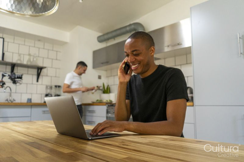 Man using laptop and phone in kitchen, boyfriend in background
