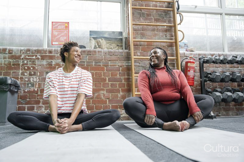 Mother and daughter stretching on mat in gym