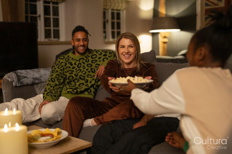 Smiling friends relaxing on sofa at home, sharing popcorn