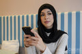 Young woman in hijab using phone in cafe