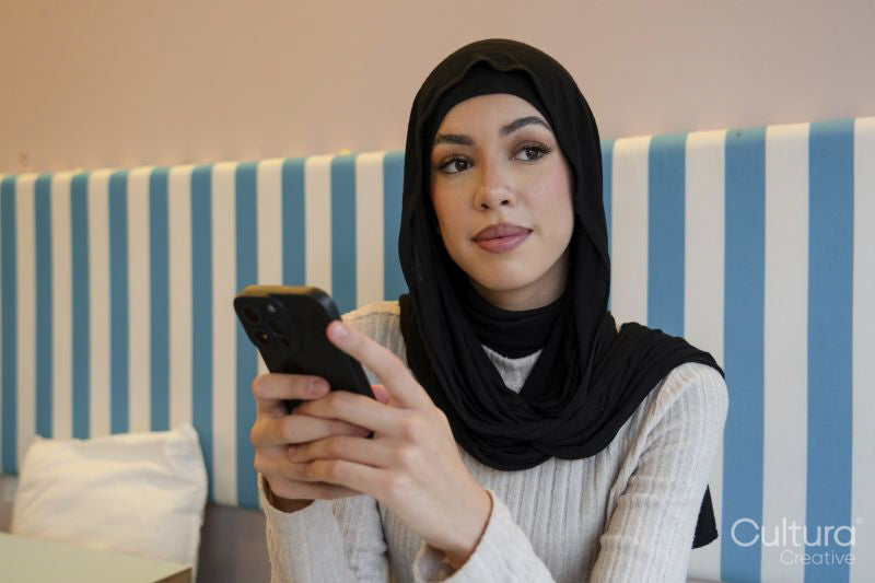 Young woman in hijab using phone in cafe