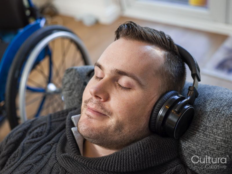 Close-up of man with headphones on sofa next to wheelchair