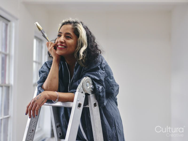 Smiling woman standing on ladder with paintbrush