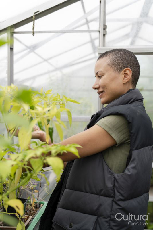 Smiling woman inspecting vegetables growing in greenhouse