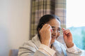 Senior lady putting on eyeglasses while sitting in chair at nursing home