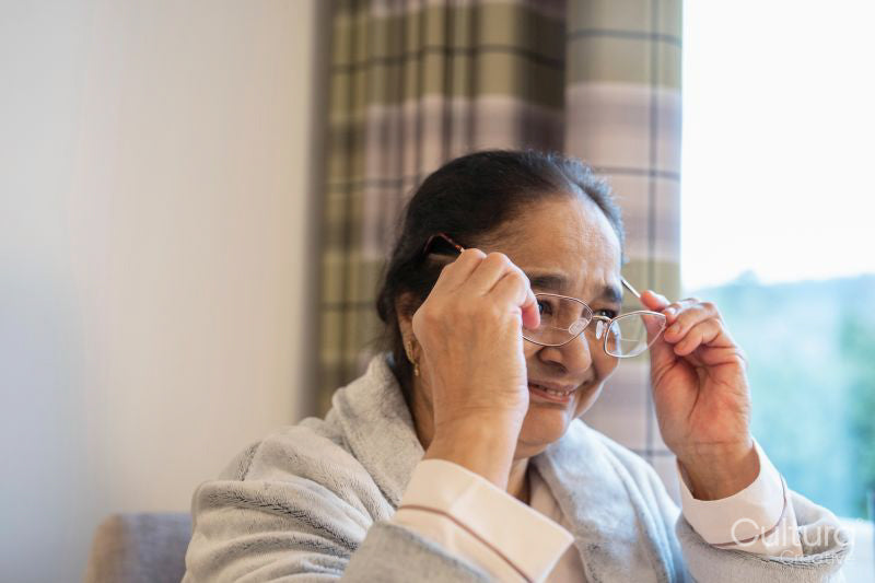 Senior lady putting on eyeglasses while sitting in chair at nursing home