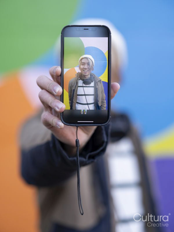Portrait of man showing photography on smart phone against colorful wall