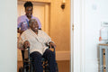 Smiling female nurse with senior woman sitting in wheelchair entering doctors office
