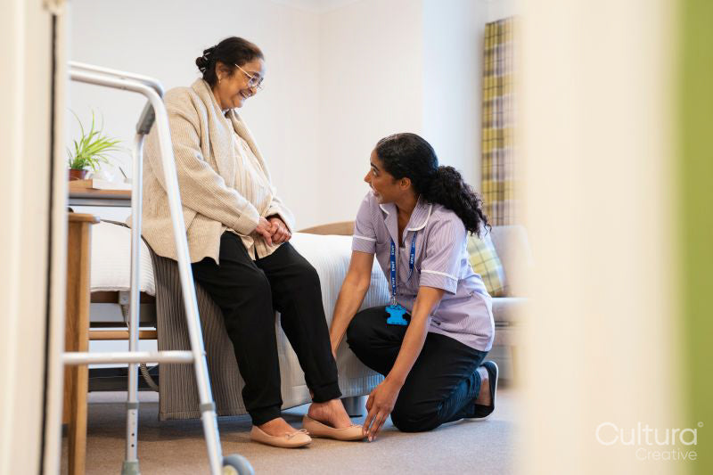 Nurse helping senior lady to put on her shoes at nursing home