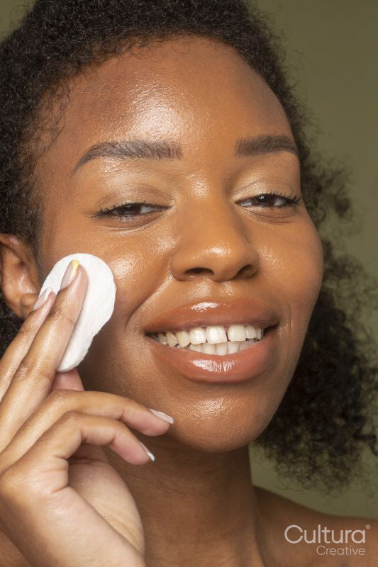 Close-up of smiling woman rubbing cheek with cotton pad