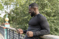 Smiling athletic man looking at smart phone on footbridge in park