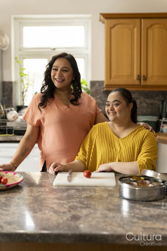 Portrait of mother with down syndrome daughter preparing food in kitchen