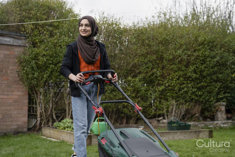 Woman wearing hijab mowing grass in backyard