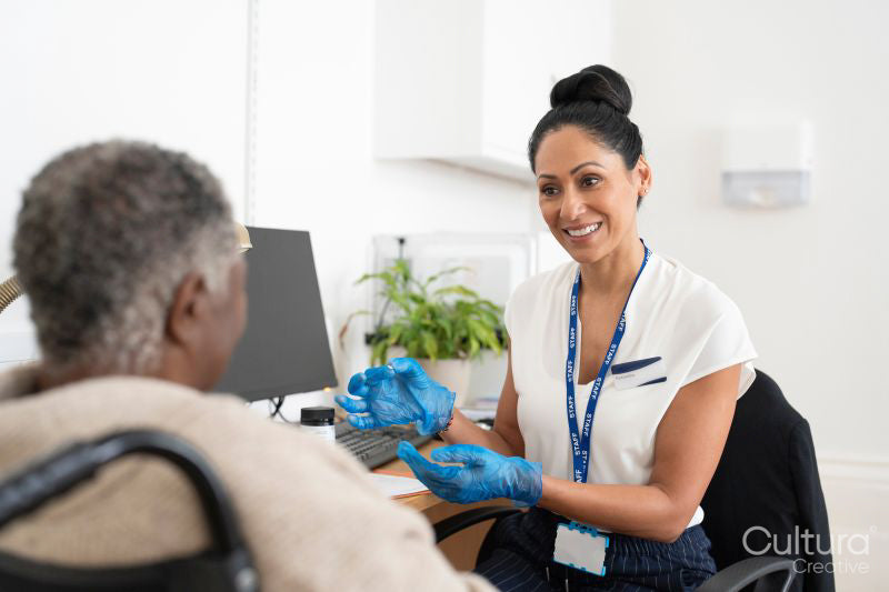 Smiling female doctor talking to senior patient sitting in wheelchair in office