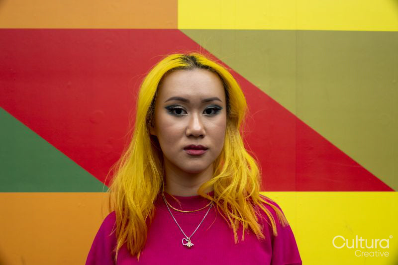 Portrait of young woman with yellow hair against colorful wall