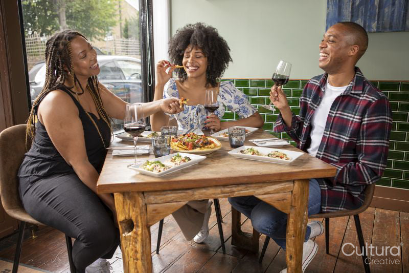 Smiling friends enjoying snacks and red wine at restaurant table