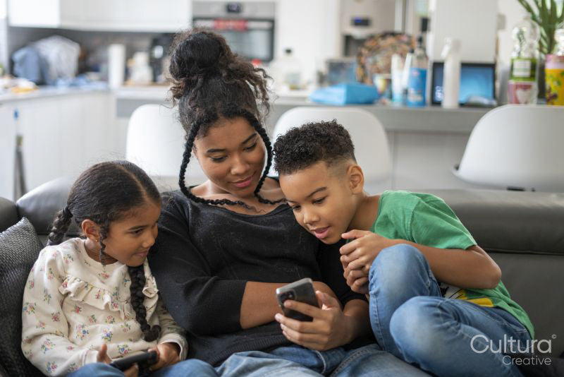 Two girls and boy sitting on sofa looking at smartphone
