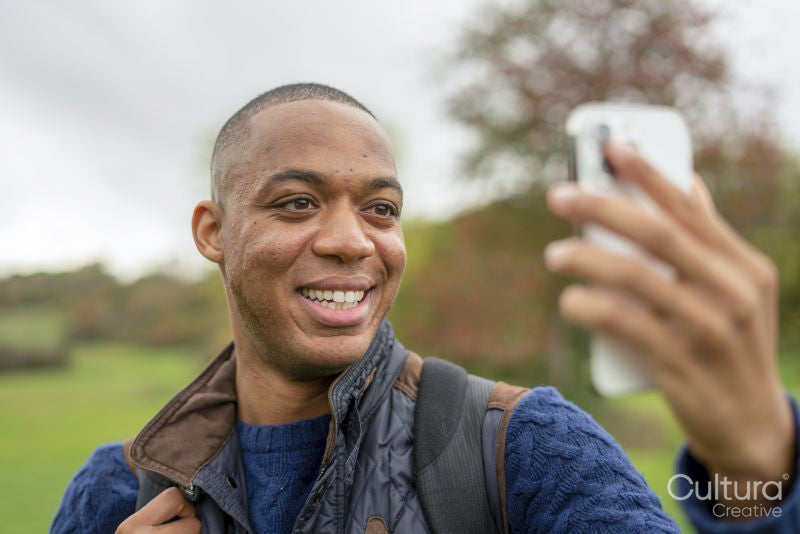 Smiling man taking selfie with smart phone in nature