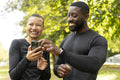 Smiling athletic man and woman looking at smart phone in park