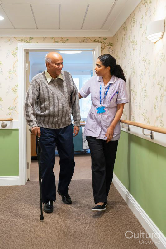 Care giver assisting senior man while walking along corridor in nursing home