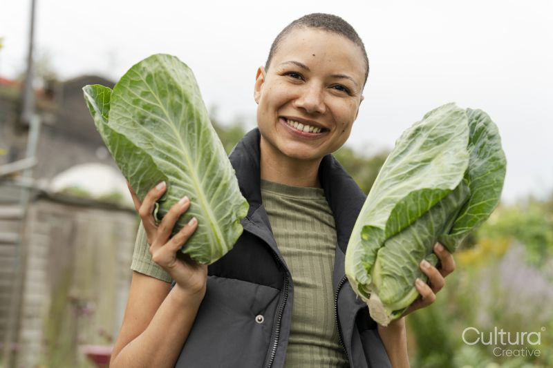 Portrait of smiling woman holding homegrown cabbages in urban garden