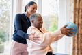 Smiling female therapist assisting senior woman exercising with ball