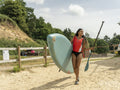 Smiling woman carrying paddleboard and oar on beach