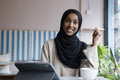 Portrait of young woman in hijab working on tablet in cafe