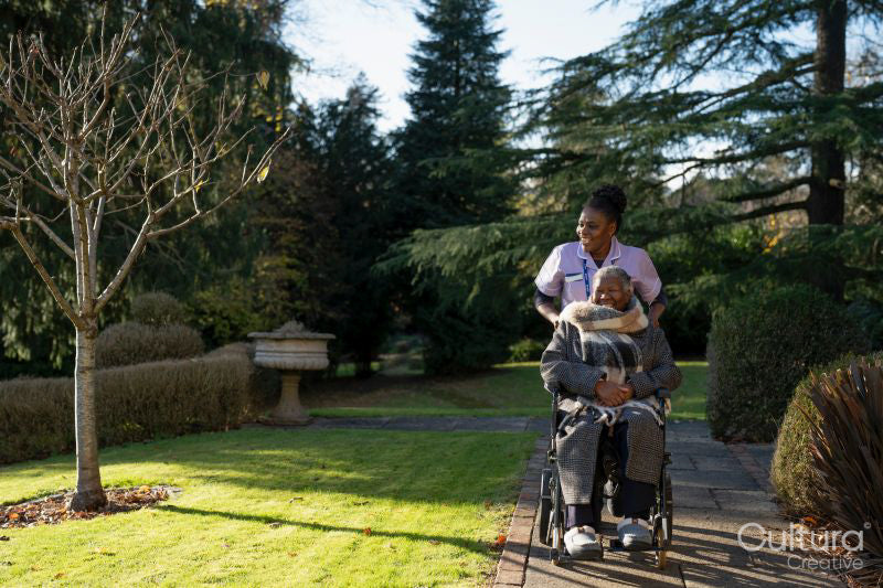 Nurse and senior woman in wheelchair going on walk in park