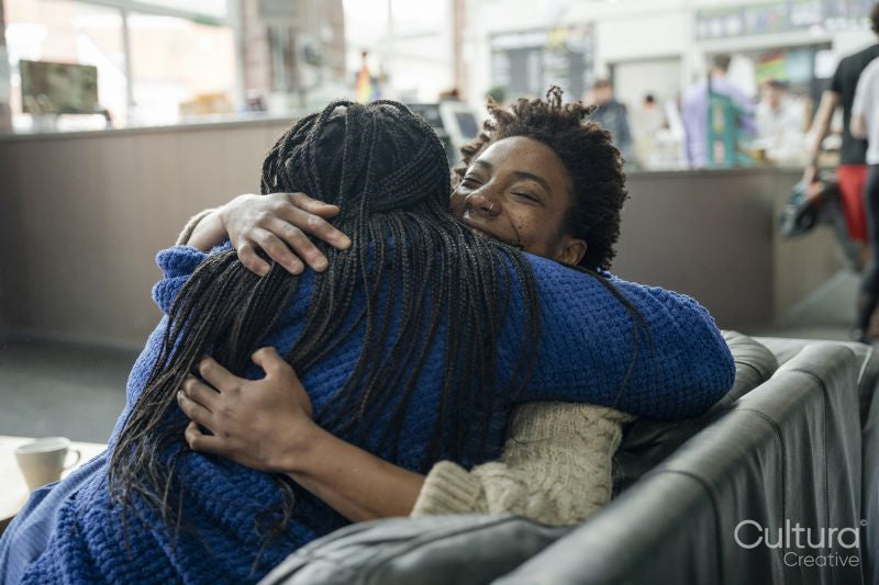 Mother with daughter embracing while sitting on sofa