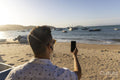 Man wearing earbuds using smart phone at beach