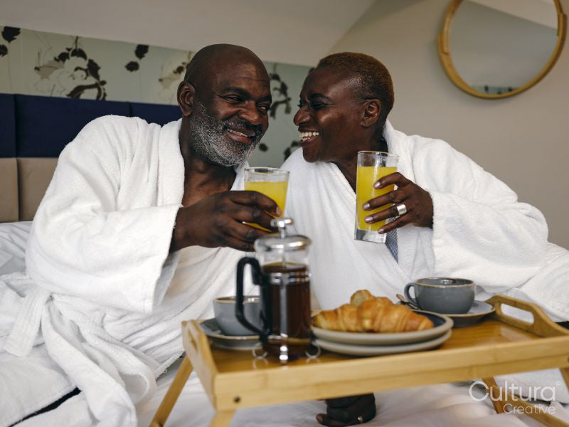 Mature couple enjoying breakfast on bed in hotel room