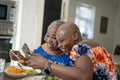 Smiling woman with adult daughter eating dinner and looking at smart phone