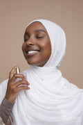 Studio shot of smiling young woman in white hijab using perfume