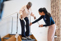 Female therapist assisting senior woman descending steps in exercise room