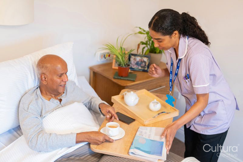 Nurse serving coffee to senior man lying in bed in room at nursing home
