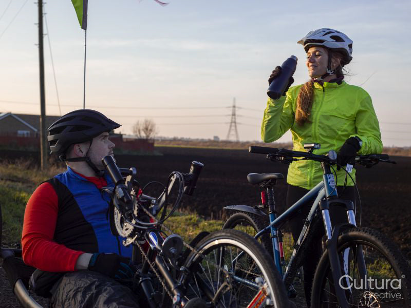 Disabled man on handcycle and woman with bicycle relaxing in rural landscape
