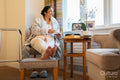 Senior lady sitting with coffee and looking through window in bedroom at nursing home