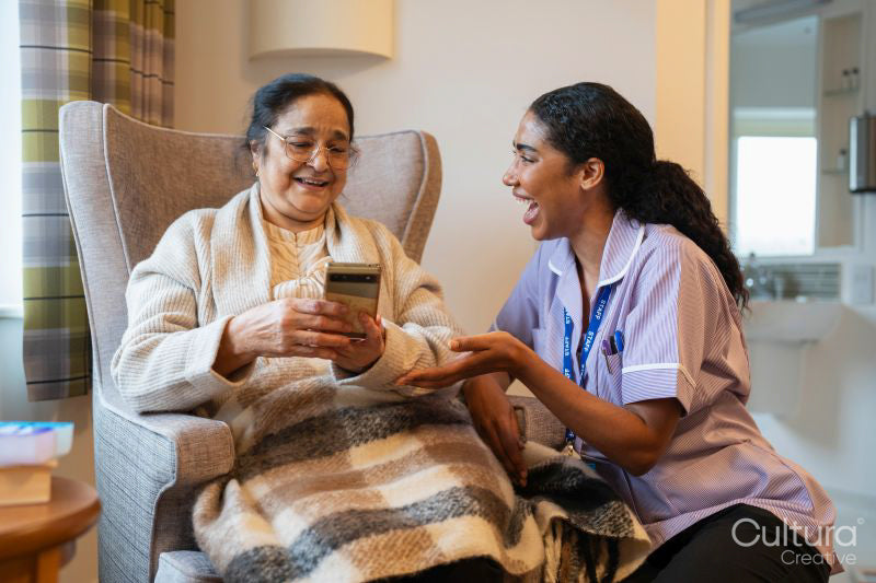 Senior lady sitting in armchair and showing phone to nurse at nursing home