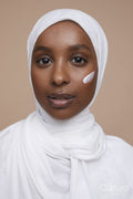 Studio portrait of young woman in white hijab applying face cream