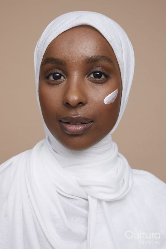 Studio portrait of young woman in white hijab applying face cream