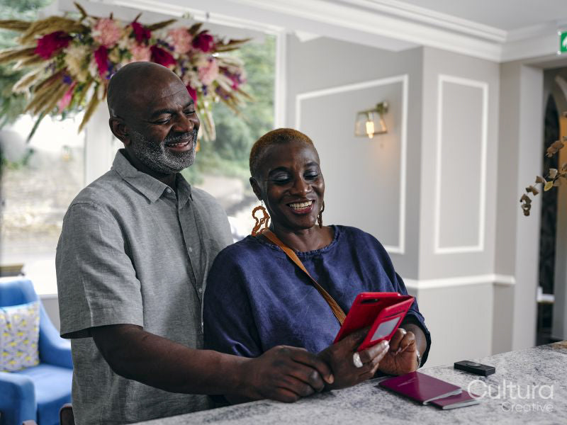 Smiling mature couple looking at smart phone at hotel front desk