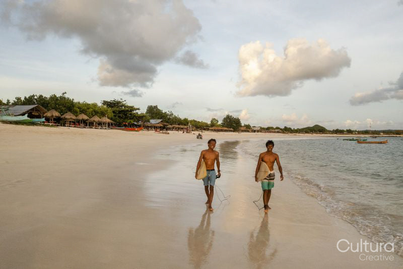Indonesia, Lombok, Surfers walking on beach at sunset