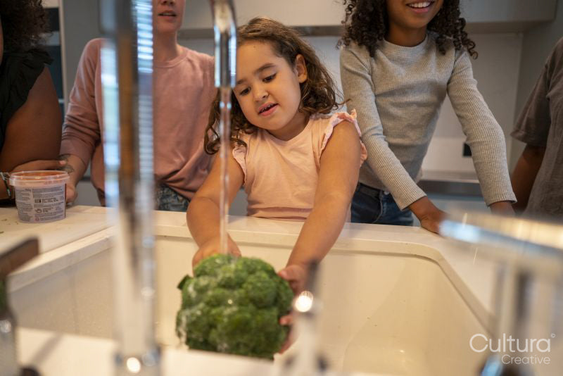 Girl washing broccoli in kitchen sink