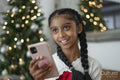 Smiling girl holding smart phone at Christmas tree