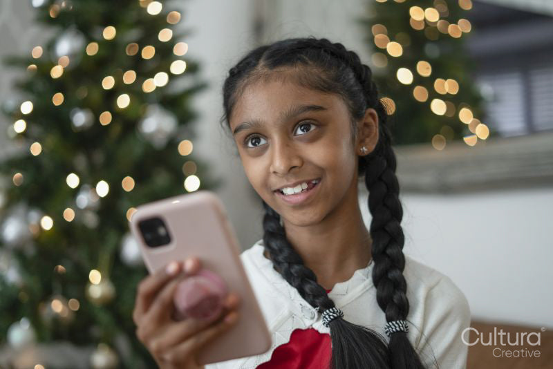 Smiling girl holding smart phone at Christmas tree