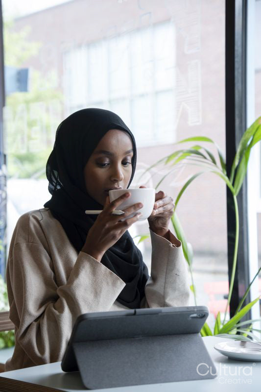 Young woman in hijab working on tablet in cafe