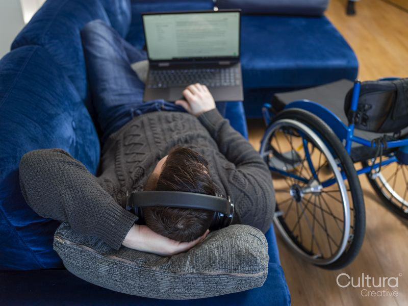 Overhead view of man with headphones and laptop on sofa next to wheelchair