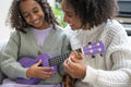 Mother assisting daughter playing ukulele at home